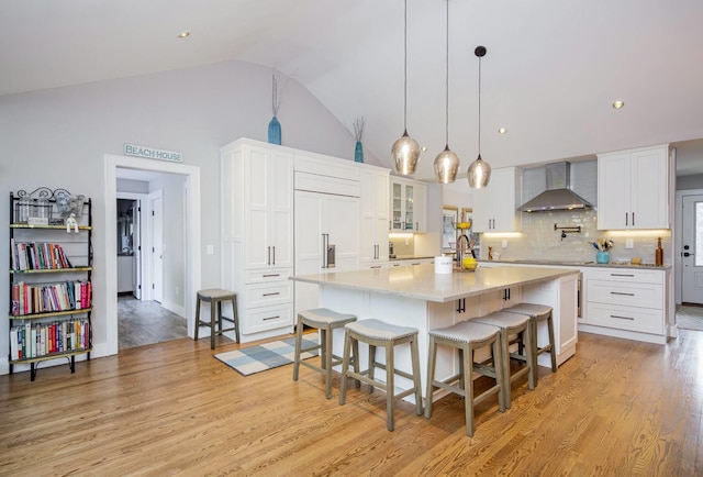 kitchen with pendant lighting, white cabinetry, wall chimney exhaust hood, a kitchen bar, and a large island with sink