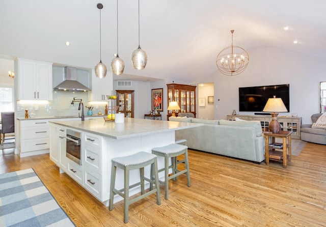 kitchen with wall chimney range hood, stainless steel oven, hanging light fixtures, and white cabinets