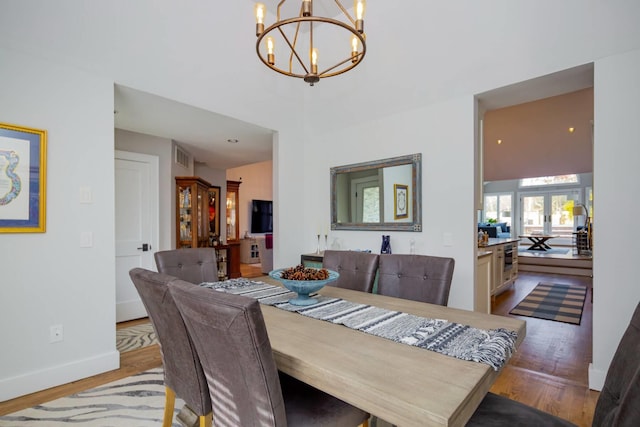 dining area with french doors, light hardwood / wood-style floors, and a notable chandelier