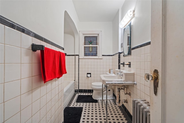 bathroom featuring a tub to relax in, toilet, radiator heating unit, and tile walls