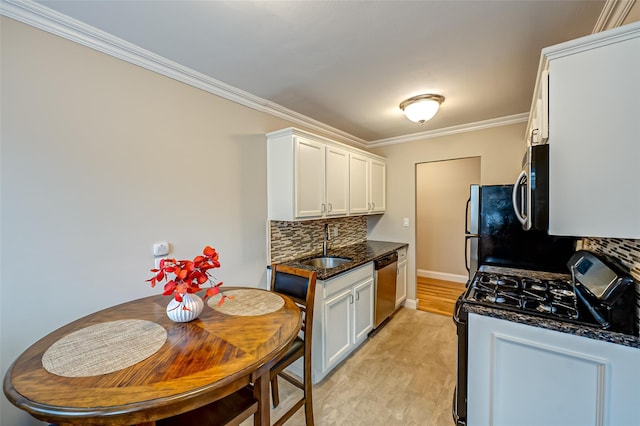 kitchen with appliances with stainless steel finishes, dark stone counters, ornamental molding, white cabinets, and sink