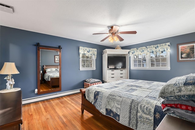 bedroom featuring hardwood / wood-style floors, a baseboard radiator, ceiling fan, a barn door, and a textured ceiling