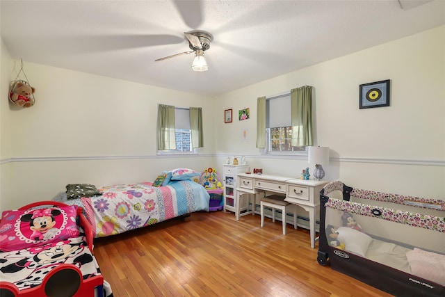 bedroom featuring hardwood / wood-style floors, a textured ceiling, ceiling fan, and baseboard heating