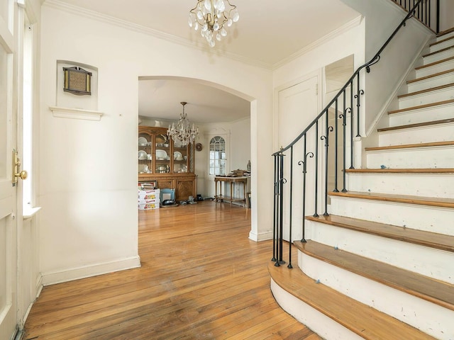 foyer entrance featuring crown molding, wood-type flooring, and a notable chandelier