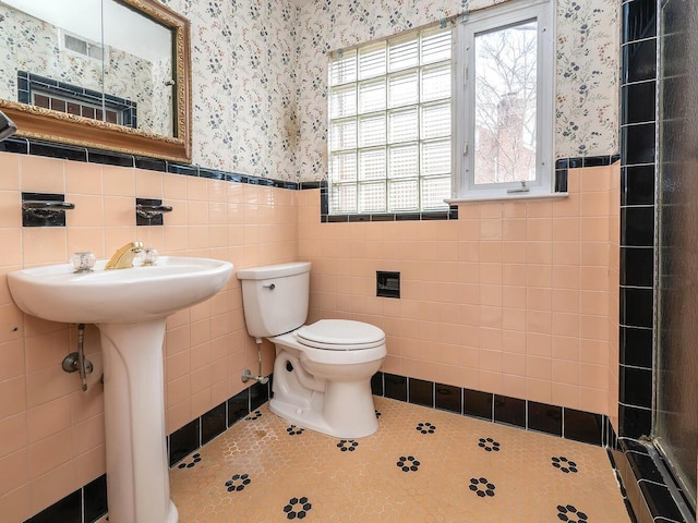 bathroom with toilet, tile walls, tile patterned flooring, and sink