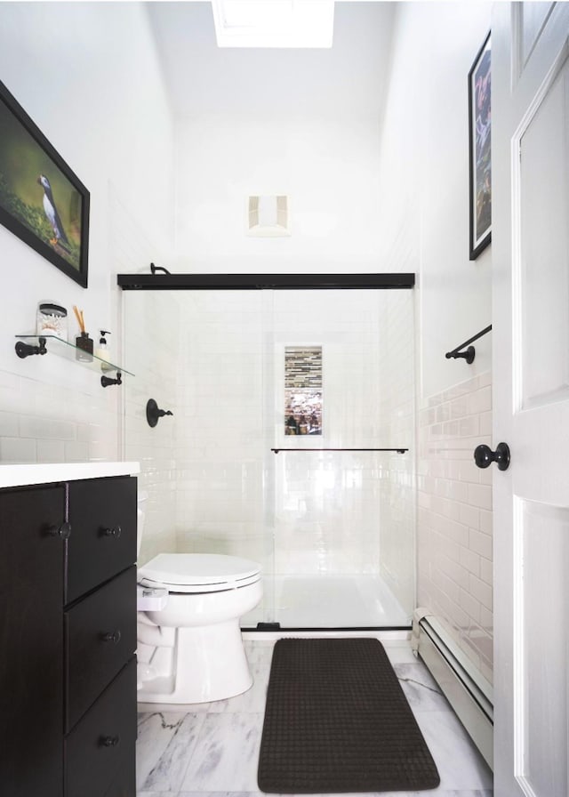 bathroom with toilet, vanity, tile walls, a baseboard heating unit, and a shower with door