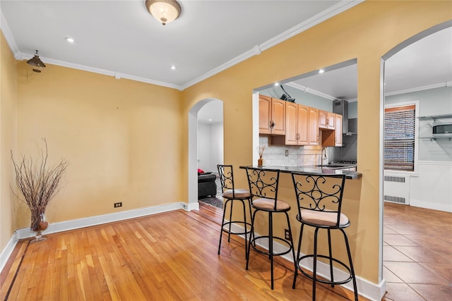 kitchen with crown molding, a breakfast bar, radiator heating unit, and tasteful backsplash