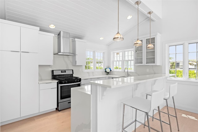 kitchen featuring a breakfast bar, stainless steel gas range oven, white cabinets, wall chimney range hood, and vaulted ceiling with beams