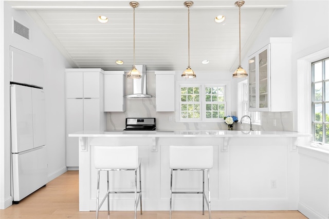 kitchen with refrigerator, white cabinetry, a breakfast bar area, and wall chimney range hood