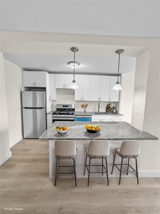 kitchen with a kitchen bar, white cabinetry, pendant lighting, and stainless steel appliances