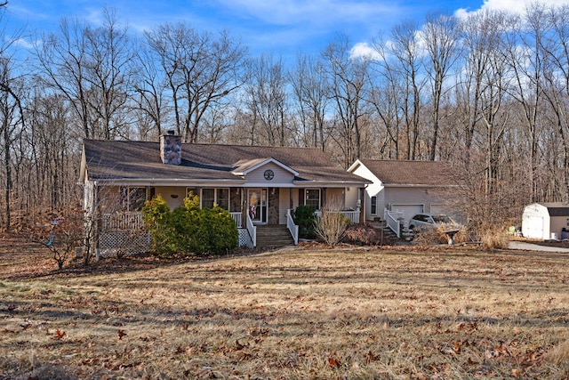 view of front facade with a shed, covered porch, an outdoor structure, an attached garage, and a chimney