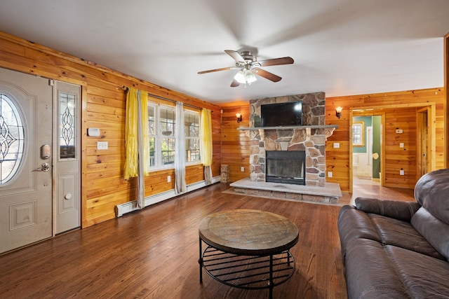 living area featuring a stone fireplace, wood finished floors, baseboard heating, and a ceiling fan