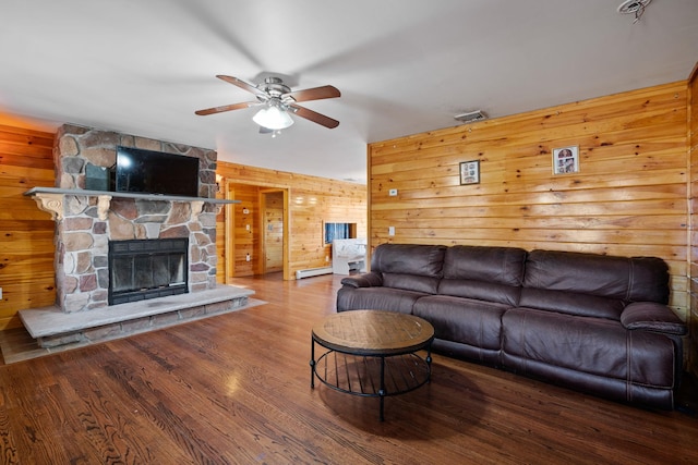 living room with baseboard heating, wood walls, ceiling fan, and a fireplace