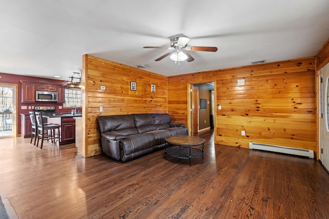 living area featuring dark wood finished floors, visible vents, a baseboard heating unit, and a ceiling fan