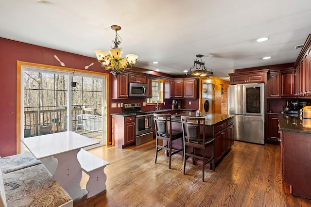 kitchen with a sink, reddish brown cabinets, dark wood-type flooring, and appliances with stainless steel finishes