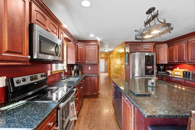 kitchen with a kitchen island, light wood-type flooring, dark stone countertops, stainless steel appliances, and a sink