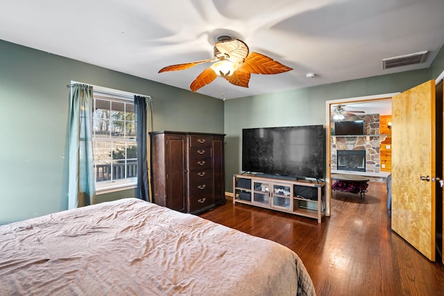 bedroom featuring ceiling fan, dark wood-type flooring, and a stone fireplace