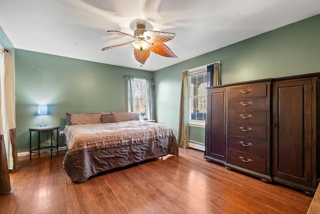 bedroom featuring ceiling fan, wood finished floors, baseboards, and a baseboard radiator