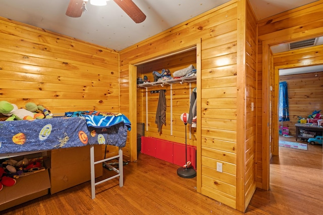 bedroom with ceiling fan, wood walls, and hardwood / wood-style flooring