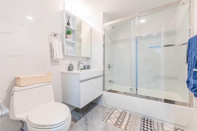 full bathroom with vanity, toilet, tile walls, and bath / shower combo with glass door