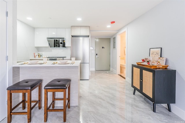 kitchen featuring a kitchen bar, stainless steel fridge, white cabinetry, and kitchen peninsula