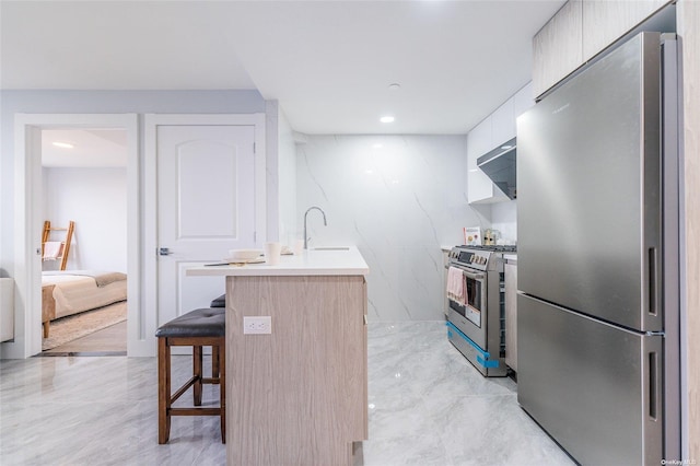 kitchen with a breakfast bar, sink, wall chimney range hood, and stainless steel appliances