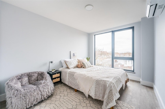 bedroom featuring light wood-type flooring, a wall unit AC, and multiple windows