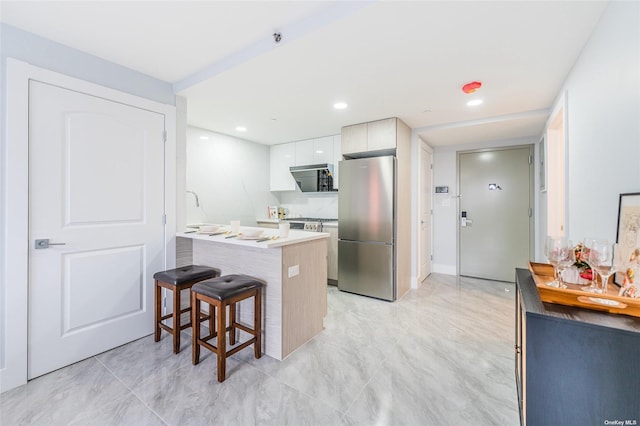 kitchen with white cabinets, kitchen peninsula, a breakfast bar area, and stainless steel refrigerator