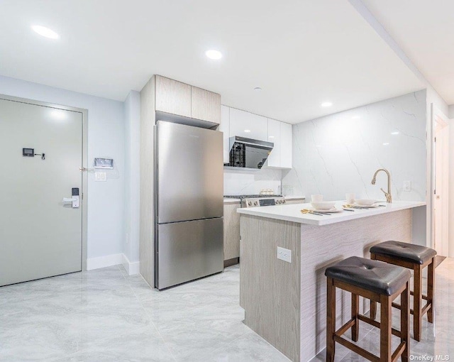 kitchen featuring stainless steel refrigerator, white cabinetry, sink, kitchen peninsula, and a breakfast bar area