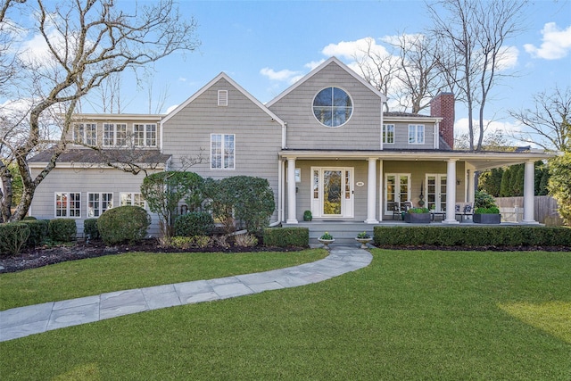 shingle-style home featuring a front yard, covered porch, and a chimney