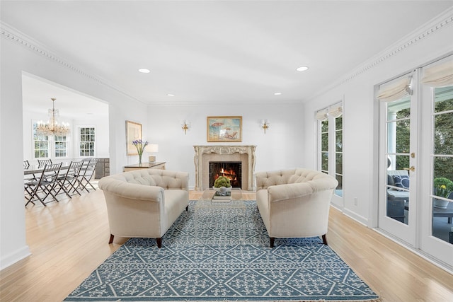 living room with a chandelier, ornamental molding, light wood-type flooring, and a high end fireplace