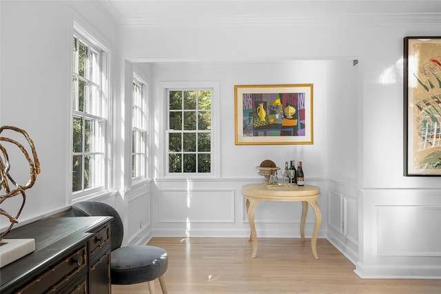 living area with light wood-type flooring, ornamental molding, and a decorative wall