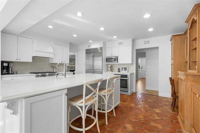 kitchen featuring tasteful backsplash, recessed lighting, light countertops, built in appliances, and premium range hood