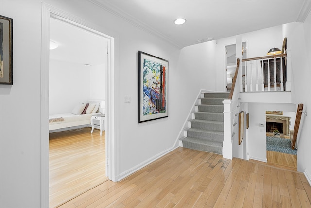 stairs featuring baseboards, hardwood / wood-style floors, crown molding, a fireplace, and recessed lighting