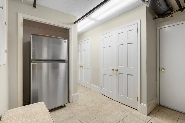 kitchen featuring light tile patterned floors, a textured ceiling, freestanding refrigerator, and baseboards