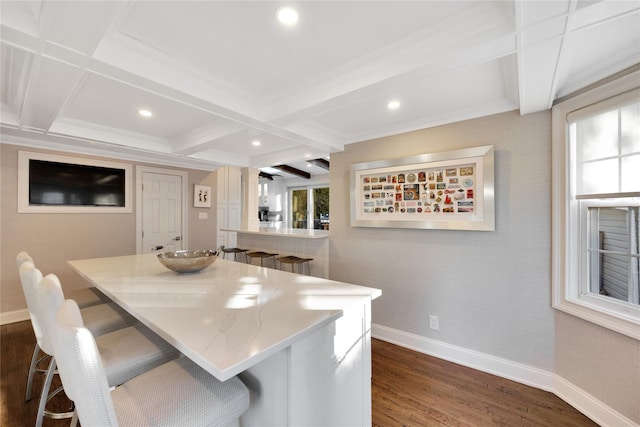 kitchen featuring dark hardwood / wood-style floors, beamed ceiling, crown molding, coffered ceiling, and a breakfast bar area