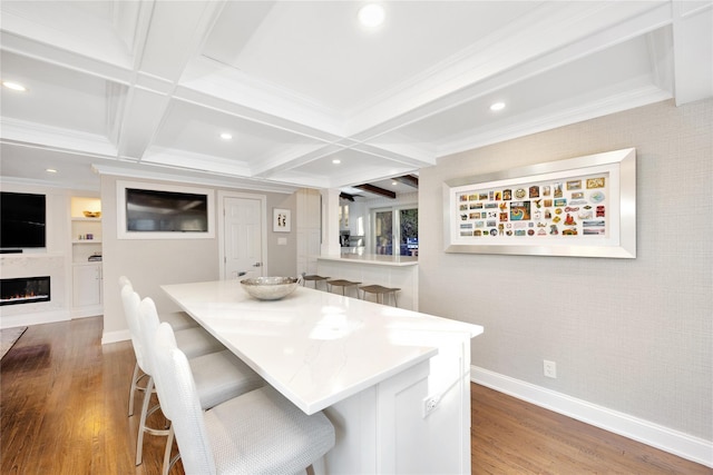 kitchen with beam ceiling, wood-type flooring, coffered ceiling, a breakfast bar area, and ornamental molding