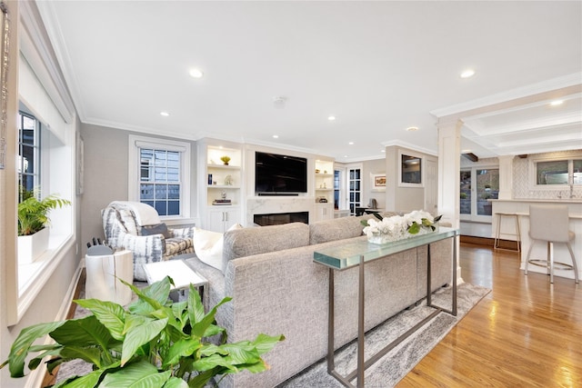 living room featuring light wood-type flooring, ornamental molding, built in features, and plenty of natural light