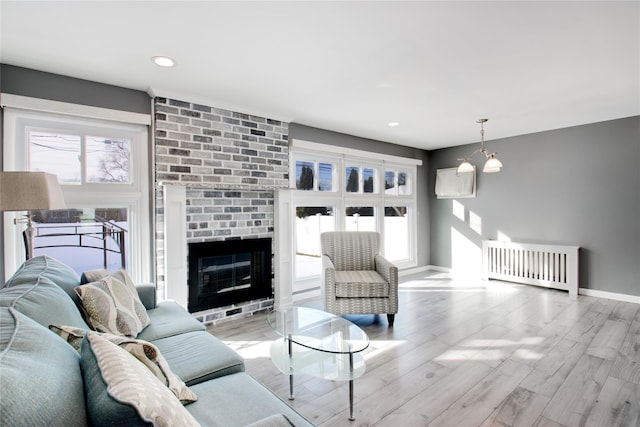 living room featuring a chandelier, a brick fireplace, and light hardwood / wood-style floors