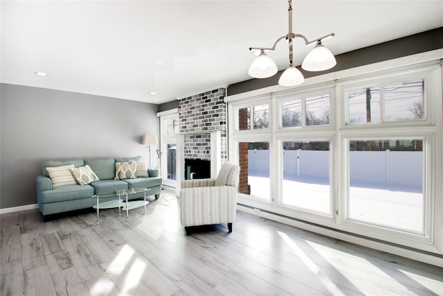 living room with light wood-type flooring, a wealth of natural light, a brick fireplace, and an inviting chandelier