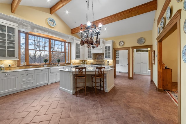 kitchen featuring decorative light fixtures, tasteful backsplash, a kitchen island, beam ceiling, and a kitchen breakfast bar