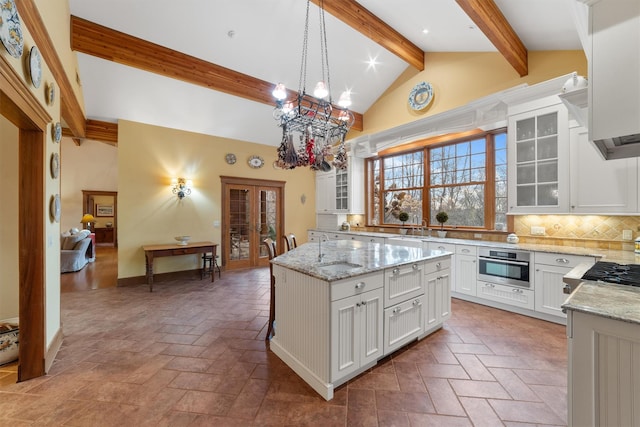 kitchen with white cabinetry, french doors, pendant lighting, backsplash, and a kitchen island with sink