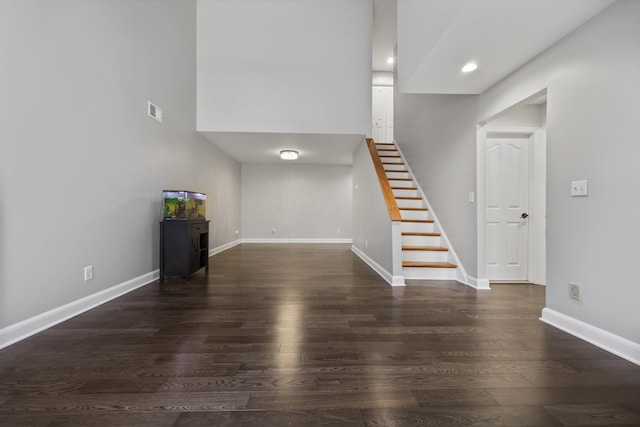 unfurnished living room featuring a towering ceiling and dark wood-type flooring