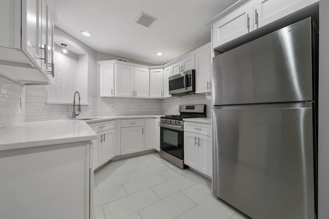 kitchen with light stone counters, stainless steel appliances, white cabinetry, and sink