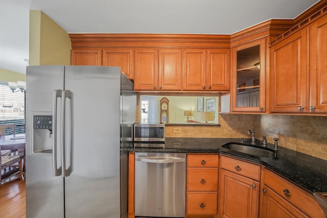 kitchen featuring appliances with stainless steel finishes, dark stone counters, decorative backsplash, sink, and light wood-type flooring