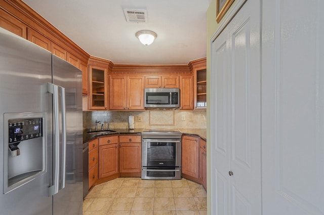 kitchen featuring light tile patterned floors, appliances with stainless steel finishes, tasteful backsplash, dark stone countertops, and sink