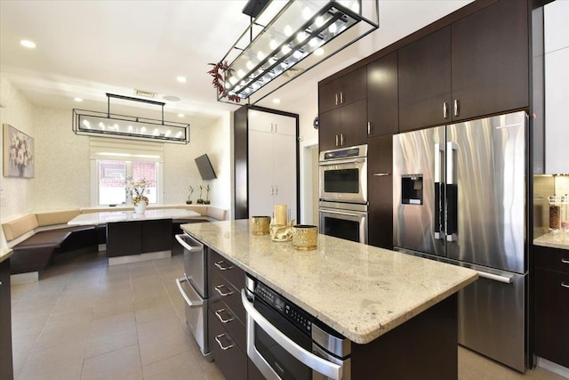 kitchen with pendant lighting, a center island, dark brown cabinetry, light stone counters, and stainless steel appliances