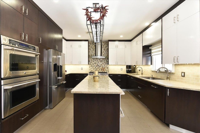 kitchen with sink, wall chimney range hood, appliances with stainless steel finishes, backsplash, and a kitchen island