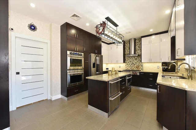 kitchen with appliances with stainless steel finishes, a kitchen island, white cabinetry, sink, and wall chimney exhaust hood