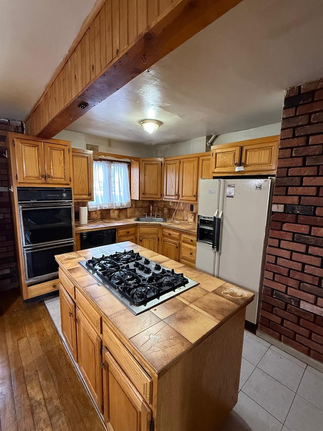 kitchen with sink, black appliances, tile counters, and a kitchen island